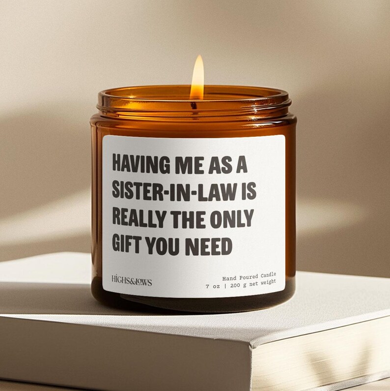 May include: A brown glass candle with a white label that reads "HAVING ME AS A SISTER-IN-LAW IS REALLY THE ONLY GIFT YOU NEED". The candle is lit and the label also includes the brand name "HIGHS&JOWS" and the text "Hand Poured Candle 7 oz | 200 g net weight".