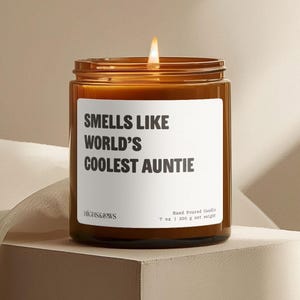 May include: A brown glass candle with a white label that reads "Smells Like World's Coolest Auntie". The candle is hand-poured and weighs 7 ounces or 200 grams.