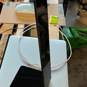 May include: A black stand with a rectangular base and a tall, thin, rectangular column. The stand is made of a glossy material and reflects the surrounding environment.