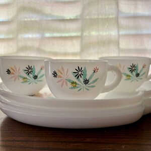 May include: Three white ceramic cups with a floral design in shades of pink, green, and black. The cups are on a white ceramic saucer.