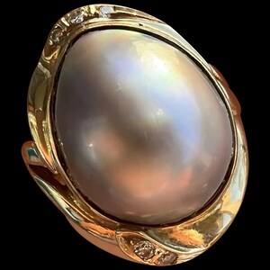May include: A gold ring with a large, iridescent pearl set in a swirling, ornate design. The ring is accented with small diamonds.