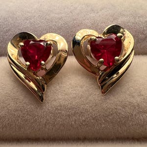 May include: A pair of gold heart-shaped earrings with red heart-shaped stones in the center.