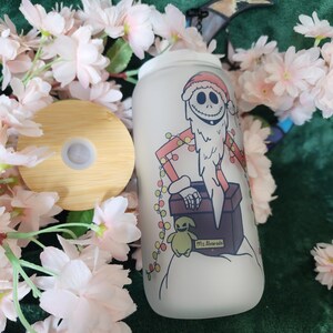May include: A frosted glass tumbler with a bamboo lid. The tumbler features a cartoon illustration of Jack Skellington in a Santa hat, with a beard and a gift box. The design includes a small Oogie Boogie character and the text "Ms. Alvarado".