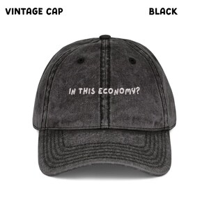 May include: Black vintage cap with the text "IN THIS ECONOMY?" embroidered in white. The cap has a curved brim and a distressed, worn look. The cap is a classic baseball style.