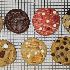 May include: Assortment of eight gourmet cookies on a wire rack. The cookies are various flavors, including chocolate chip, pecan, and strawberry.