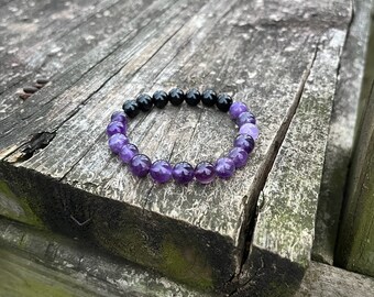 May include: A purple and black beaded bracelet with a graduated colour pattern. The bracelet is made of amethyst and black onyx beads.