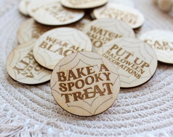 May include: Wooden circle game pieces with various Halloween-themed phrases, including "Bake a Spooky Treat", "Put Up Halloween Decorations", "Wear All Black", and "Carve Pumpkins".