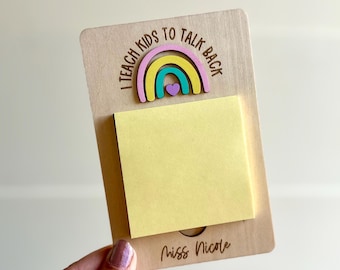 May include: Wooden notepad holder with a rainbow design and the text "I teach kids to talk back." A yellow sticky note pad is attached. The name "Miss Nicole" is written at the bottom.