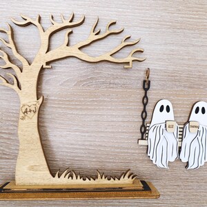 May include: Wooden Halloween-themed decor featuring a tree with initials and a heart, and two ghost figures on a swing. The ghosts hold mugs with the words "All" and "Together". The tree has a base with grass.