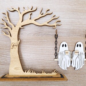 May include: Wooden tree and swing set decoration. The tree has a heart with "A+J" carved into it. Two white ghost figures are on a swing, each holding a cup. The words "ALID" and "TOGETHER" are on the cups.