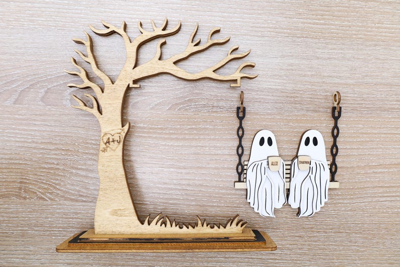 May include: Wooden tree and swing set decoration. The tree has a heart with "A+J" carved into it. Two white ghost figures are on a swing, each holding a cup. The words "ALID" and "TOGETHER" are on the cups.