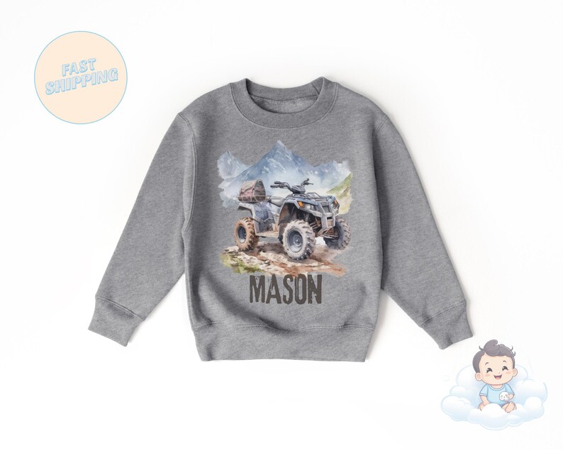 K&ouml;nnte beinhalten: Graues Sweatshirt mit Aquarell-Illustration eines ATVs und Berglandschaft. Der Name "MASON" ist in Braun unter dem ATV aufgedruckt. Das Sweatshirt hat einen Rundhalsausschnitt.