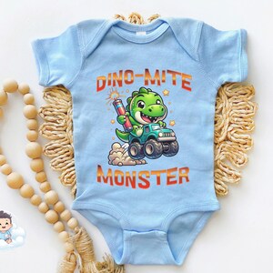 May include: A light blue baby onesie with a green dinosaur wearing a blue monster truck and holding a red firework. The text "Dino-mite Monster" is printed in orange on the onesie.