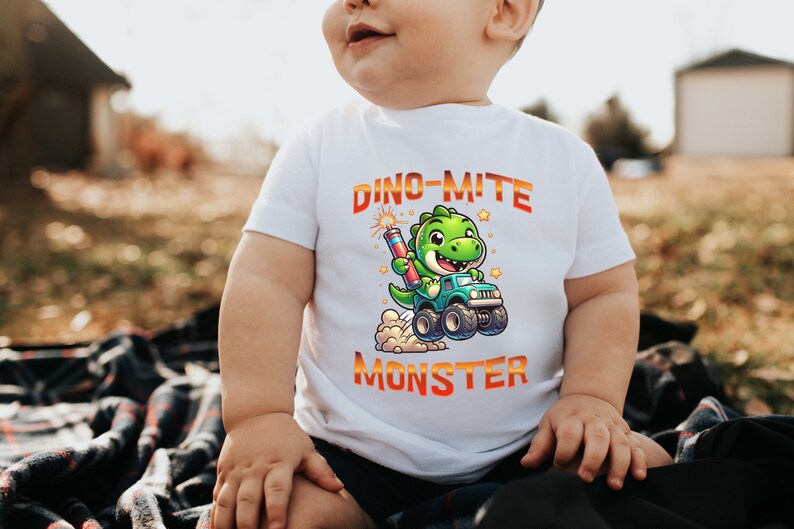 May include: A white t-shirt with a green dinosaur holding a firework and driving a monster truck. The text on the shirt reads "Dino-mite Monster".