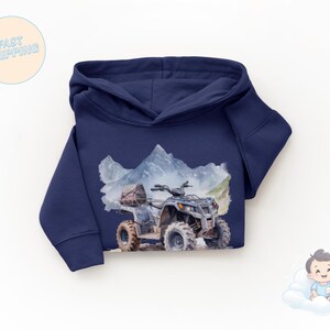 K&ouml;nnte beinhalten: Marineblauer Kapuzenpullover mit einer Aquarellillustration eines ATVs vor einer Berglandschaft. Das ATV ist grau und braun, mit einem Gep&auml;cktr&auml;ger. Der Kapuzenpullover ist ein bequemer, l&auml;ssiger Stil.