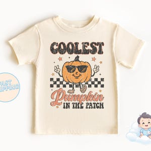 Op de afbeelding: Een crèmekleurig T-shirt met een vintage stijl afbeelding van een pompoen met een zonnebril en de tekst "Coolest Pumpkin in the Patch".