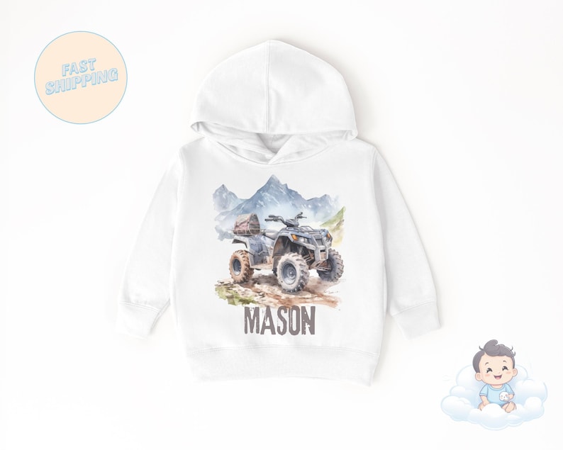 K&ouml;nnte beinhalten: Wei&szlig;er Kapuzenpullover mit einer Aquarellillustration eines Quads auf einem Feldweg, mit Bergen im Hintergrund. Der Name "MASON" ist in braunen Blockbuchstaben aufgedruckt. Der Pullover hat ein klassisches Design.