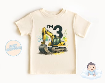 Könnte beinhalten: Ein hellgelbes T-Shirt mit einem Aufdruck eines gelben Baggers und dem Text "I'm 3" in Schwarz. Der Bagger befindet sich auf einem Erdhintergrund mit grünen und blauen Aquarellspritzer.