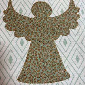 May include: A fabric angel applique with outstretched wings, featuring a green and brown floral pattern. The angel is set against a white background with a diamond pattern in light green. This decorative piece is suitable for crafts and home decor.