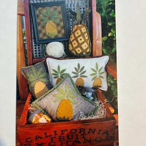 May include: A wooden crate filled with decorative pineapple-themed pillows, a framed picture, and a stuffed pineapple. The crate has the words "CALIFORNIA FRUIT EXCHANGE" printed on the side. The pillows and picture feature a yellow and green pineapple design.