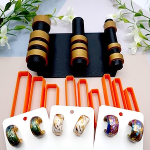 Peut inclure: Six paires de créoles colorées présentées sur une carte blanche avec un fond noir. Les boucles d'oreilles sont en verre et présentent une variété de motifs et de couleurs.