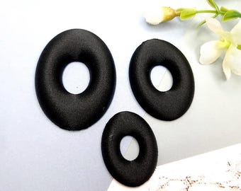 May include: Three black fabric donut shapes of varying sizes. The donuts are flat and have a smooth, velvety texture.