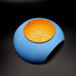 Puede incluir: Una cúpula decorativa azul y dorada con un patrón de espiral en la parte superior. La cúpula está hecha de un material texturizado.