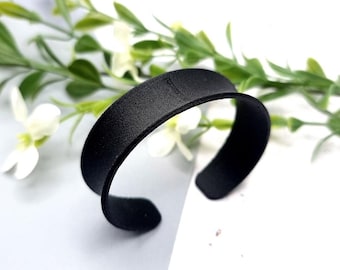 Peut inclure: Un bracelet jonc en cuir noir avec une finition lisse et mate.