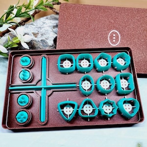 May include: A teal blue plastic tray with a variety of button shapes and sizes. The tray is divided into sections and has a small, teal blue handle. The tray is open and the buttons are visible.
