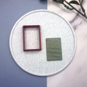 Può includere: Due timbri in pasta polimerica su una superficie bianca macchiata. Un timbro è una cornice rettangolare rossa, l'altro è un timbro verde con un motivo paisley.