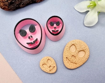 May include: Four pink and brown cookie cutters shaped like alien faces. The cutters are different sizes and have black details.