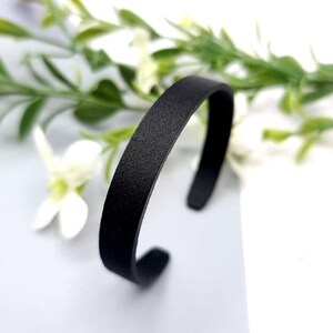 Op de afbeelding: Een zwarte leren armband met een gladde, matte afwerking.