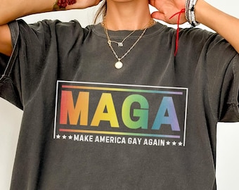 May include: A dark gray oversized t-shirt with a rainbow colored "Maga" graphic and the text "Make America Gay Again" printed on the front.