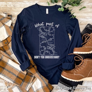 May include: Navy blue long-sleeve t-shirt with a white graphic of a maze with the text "What part of don't you understand?"  The shirt is laying on a plaid fabric and brown leather boots.