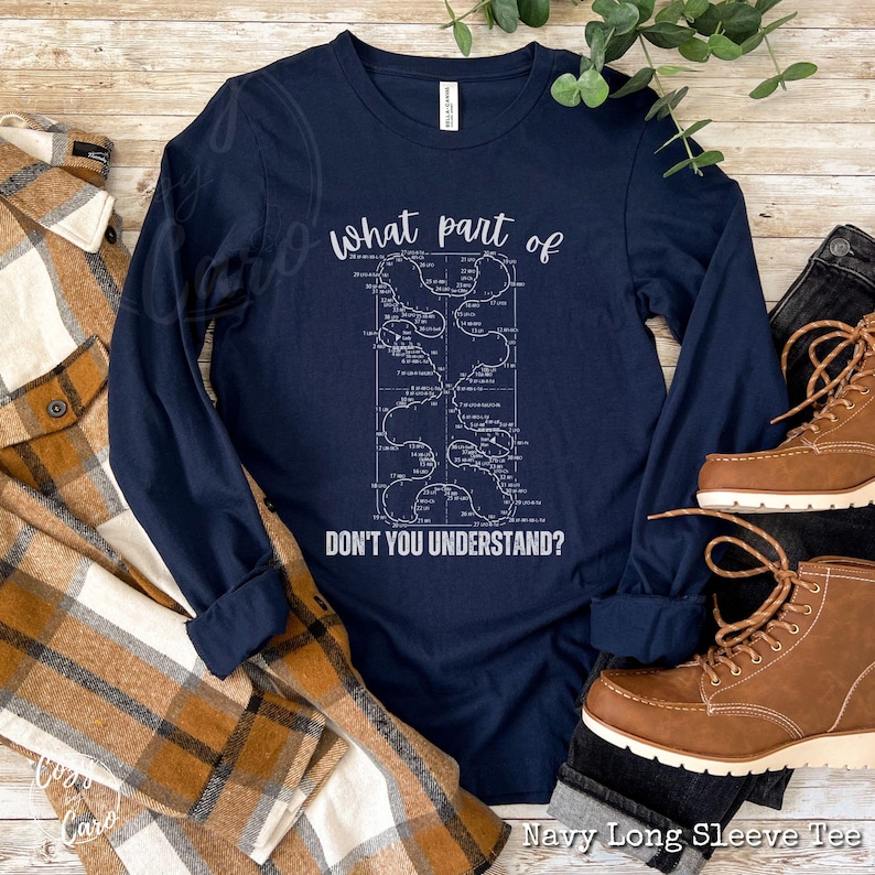 May include: Navy blue long-sleeve t-shirt with a white graphic of a maze with the text "What part of don't you understand?"  The shirt is laying on a plaid fabric and brown leather boots.