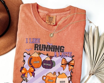 May include: Orange Comfort Colors t-shirt with the phrase "I Like Running A Latte" and pumpkin-themed graphics. The shirt features a gold necklace and a brown hat. The design includes pumpkins, coffee cups, and bows.