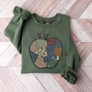 Könnte beinhalten: Grünes Sweatshirt mit einem Apfel-Design. Der Apfel besteht aus Patchwork-Stoffen, darunter Vichy, Blumenmuster und Punkte. Das Sweatshirt hat lange Ärmel und einen Rundhalsausschnitt.