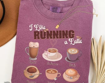 May include: Berry-colored t-shirt with the phrase "I Like Running a Latte" and coffee-themed graphics. The shirt features various coffee cup illustrations with words like "Sprint" and "Endurance". A gold necklace and a brown hat are also visible.