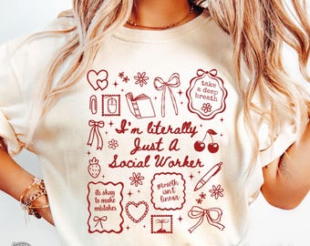 Op de afbeelding: Ivoor Comfort Colors T-shirt met een rood grafisch ontwerp. Het ontwerp bevat de tekst "I'm literally Just a Social Worker" omringd door verschillende illustraties zoals harten, bloemen en strikken. Het shirt heeft ook de tekst "take a deep breath".