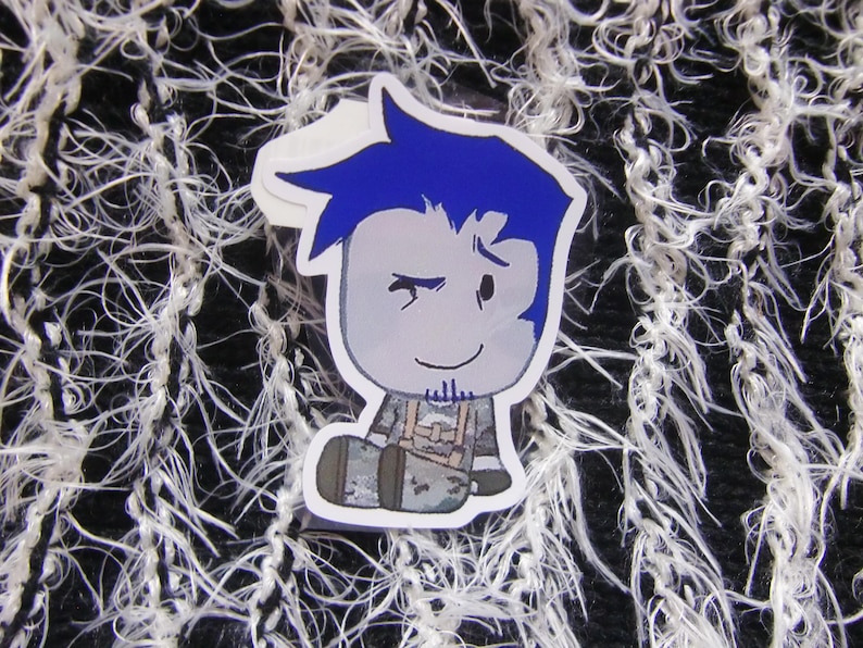 Puede incluir: Una pegatina con un personaje de dibujos animados con pelo azul y una expresi&oacute;n gui&ntilde;ando un ojo. El personaje lleva un atuendo gris con un arn&eacute;s. La pegatina est&aacute; sobre un fondo texturizado en blanco y negro.