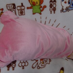 Puede incluir: Una almohada de felpa rosa con forma de cabeza de oso. La almohada tiene una textura suave y aterciopelada y est&aacute; sobre un fondo blanco con personajes de dibujos animados impresos en ella. La almohada tiene una etiqueta adjunta que dice "まめねこ" en japon&eacute;s.