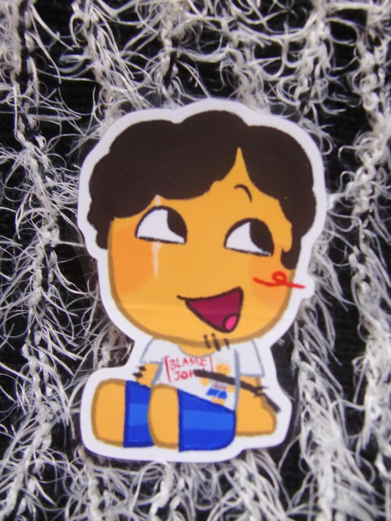 Puede incluir: Una pegatina con un personaje de dibujos animados con pelo casta&ntilde;o, cara naranja y pantalones cortos azules. El personaje sonr&iacute;e con la boca roja y una l&iacute;nea roja en la nariz. La camiseta dice "BLAKE 301".