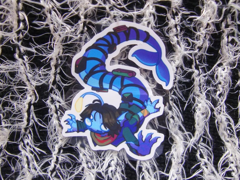 Puede incluir: Una pegatina con un personaje de dibujos animados con cuerpo azul, pelo oscuro y una luz amarilla brillante. El personaje tiene una cola de pez y lleva una bufanda verde y roja. La pegatina est&aacute; sobre un fondo blanco y negro texturizado.