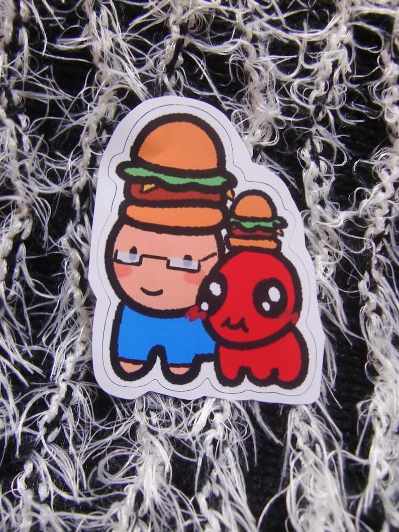 Puede incluir: Una pegatina con dos personajes de dibujos animados con hamburguesas en la cabeza. Un personaje es una persona con gafas y pantalones cortos azules, y el otro es una criatura roja. La pegatina tiene un borde blanco.