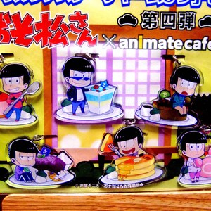 May include: A collection of acrylic keychains featuring cartoon characters with desserts. Each keychain depicts a character with a different dessert, such as cake, pancakes, and a roll cake. The keychains have a clear background and are attached to a display.
