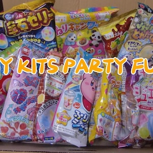 Może przedstawiać: Kartonowe pudełko wypełnione kolorowymi zestawami DIY ze słodyczami i jedzeniem. Opakowania zawierają japoński tekst i postacie z kreskówek. Tekst "DIY KITS PARTY FUN" jest wyświetlany żółtą i pomarańczową czcionką.