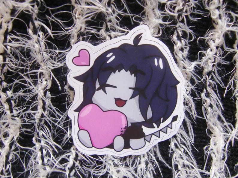 Puede incluir: Una pegatina con un personaje de estilo anime con cabello azul oscuro, sosteniendo un coraz&oacute;n rosa. El personaje tiene una expresi&oacute;n sonriente y est&aacute; sobre un borde blanco. Un peque&ntilde;o coraz&oacute;n rosa flota sobre la cabeza del personaje.