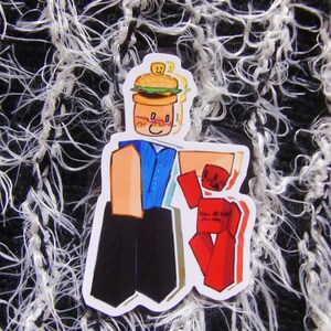 Puede incluir: Una pegatina con un personaje de dibujos animados con cabeza de hamburguesa, sosteniendo una figura de bloque rojo. El personaje lleva una camisa azul y pantalones negros. La figura roja tiene texto. Fondo texturizado en blanco y negro.