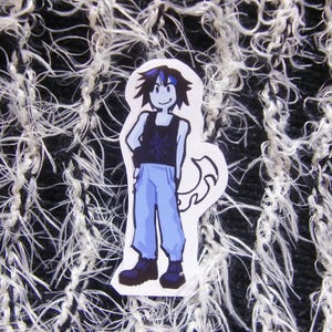 Puede incluir: Una pegatina con un personaje de dibujos animados con una camiseta sin mangas negra con un dise&ntilde;o de copo de nieve, pantalones azules y botas negras. El personaje tiene el pelo negro y azul y est&aacute; de pie con una mano en la cadera. Fondo texturizado en blanco y negro.