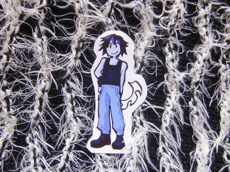 Puede incluir: Una pegatina con un personaje de dibujos animados con una camiseta sin mangas negra con un dise&ntilde;o de copo de nieve, pantalones azules y botas negras. El personaje tiene el pelo negro y azul y est&aacute; de pie con una mano en la cadera. Fondo texturizado en blanco y negro.